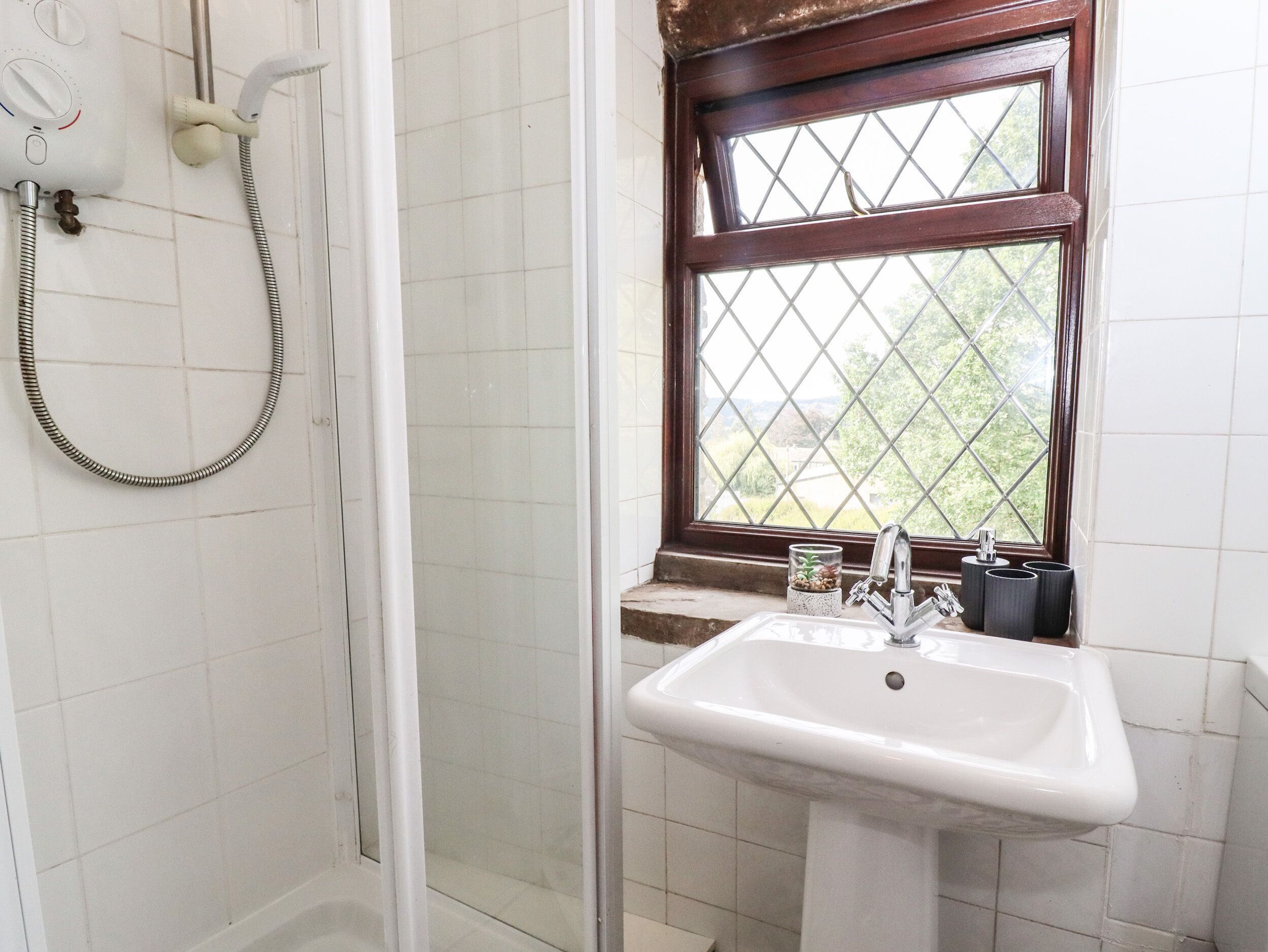 A bathroom with a shower, a sink, and a window with a view of greenery.