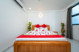 Una cama bien tendida con una colcha rojo y blanco, un cabecero de madera y almohadas rojas. Hay dos mesitas de noche con plantas decorativas.
