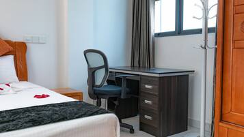 A hotel room with a bed, a desk, a chair, a coat rack, and a window.