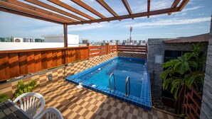Una piscina en la azotea con piso a cuadros, pérgola de madera y vistas de la ciudad.