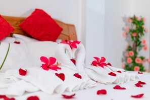 Una cama bien hecha con almohadas rojas, un ramo de flores rojas y una pared decorativa con flores rosas.