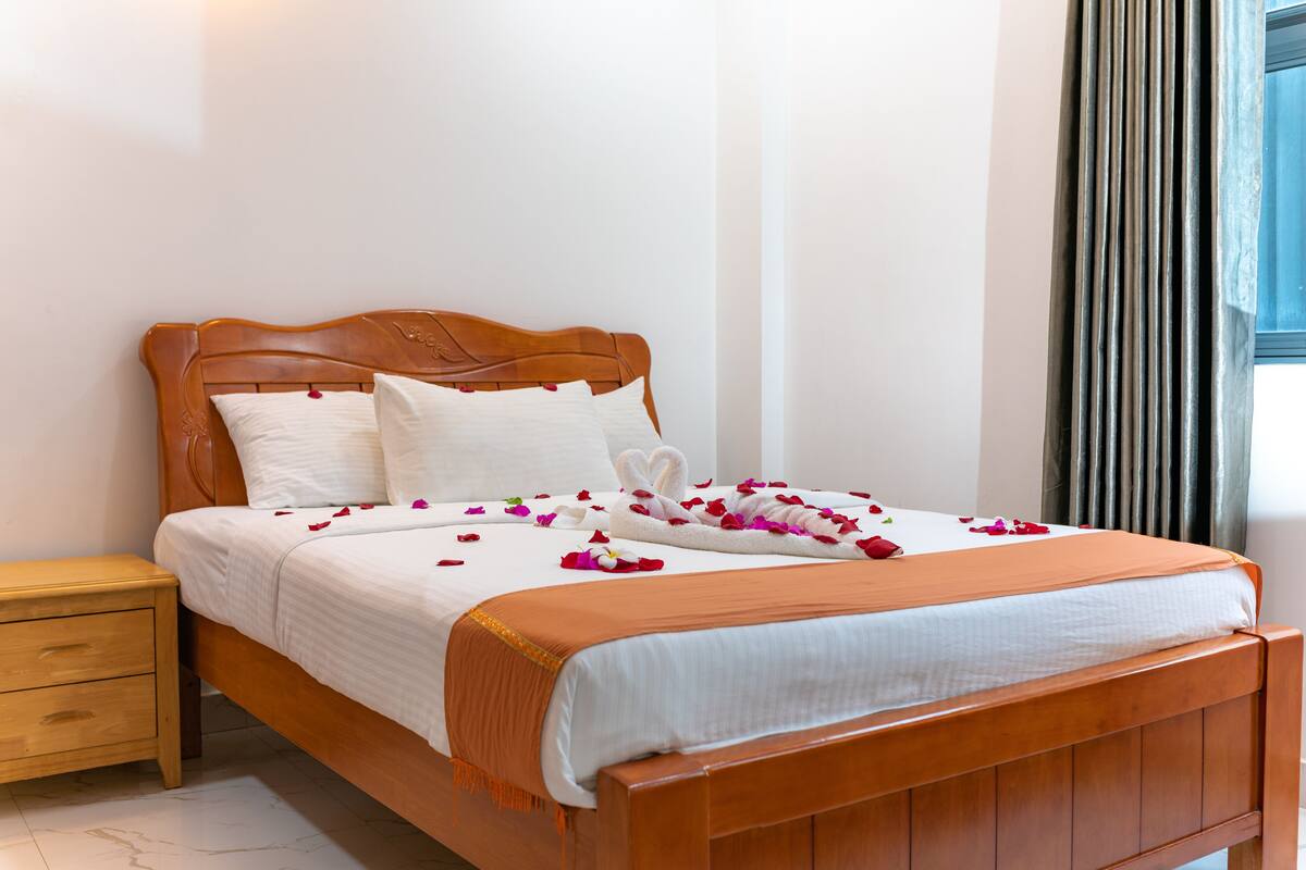A neatly made bed with a wooden headboard, white linens, and rose petals.