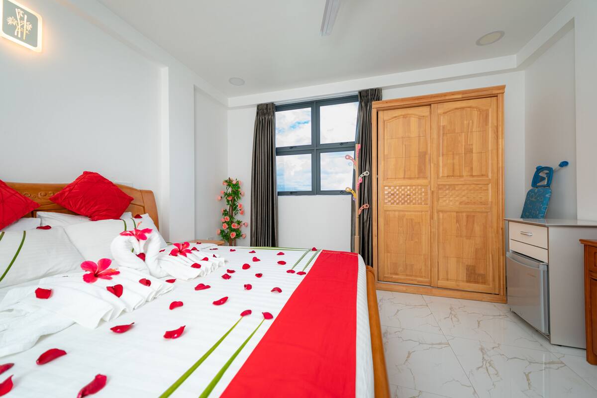 A hotel room with a bed, a wardrobe, a small kitchenette, and a window with curtains.
