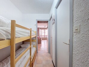 A narrow hallway with bunk beds on the left, a door on the right, and a view into a room with a window and a door at the end. - Studio for 4 pers with south balcony near shops and slopes (Montvalezan-La Rosière)