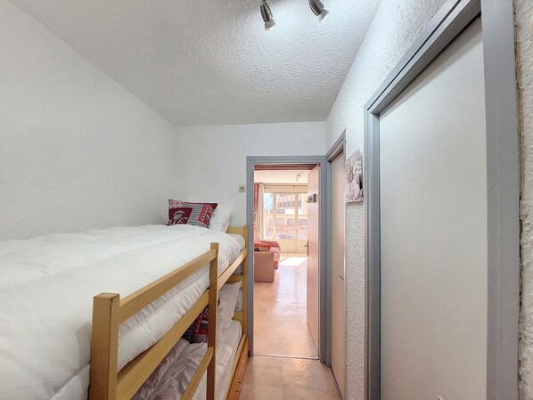 Una habitación pequeña con una cama individual en literas de madera, techo blanco y puerta que da a un pasillo.