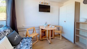 A compact living space with a sofa, a small dining table with chairs, a TV mounted on the wall, and a white wardrobe. - Renovated Studio 3 pers. - Ski-in Ski-out with Balcony (Les Menuires)