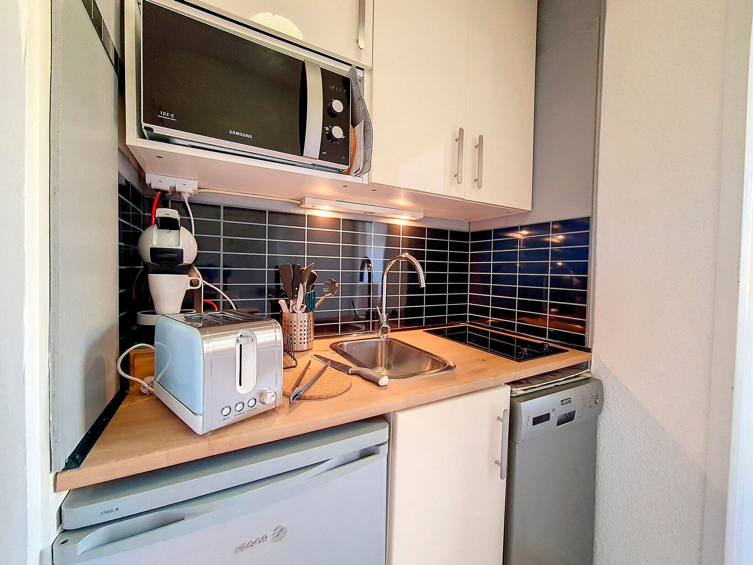 Una kitchenette compacta equipada con microondas, tostadora, pileta y lavavajillas.