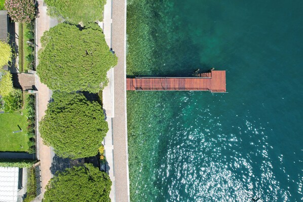 Vista aérea de un muelle que se adentra en aguas azules y cristalinas, rodeado de frondosos árboles verdes y un sendero pavimentado.