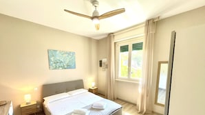 A bedroom with a bed, bedside lamps, a ceiling fan, a window with curtains, and a painting on the wall. - Lakefront villa with secular park, private jetty and pool 10 km from Salò (Toscolano Maderno)