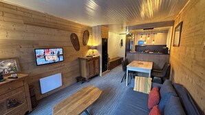 L’intérieur chaleureux d’un chalet avec une table à manger en bois, un canapé et un téléviseur fixé au mur.