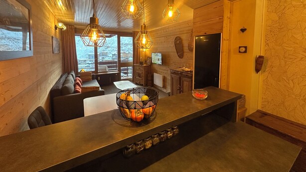 Un intérieur de chalet chaleureux avec des murs en bois, une grande fenêtre, un coin repas et une cuisine.