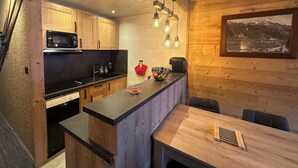 Une cuisine compacte avec des meubles en bois, un plan de travail noir et un coin repas comprenant une table et des chaises.