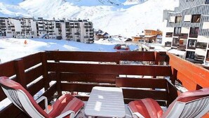 Un paysage montagneux enneigé, avec des bâtiments modernes et une terrasse en bois dotée de chaises et d’une table.