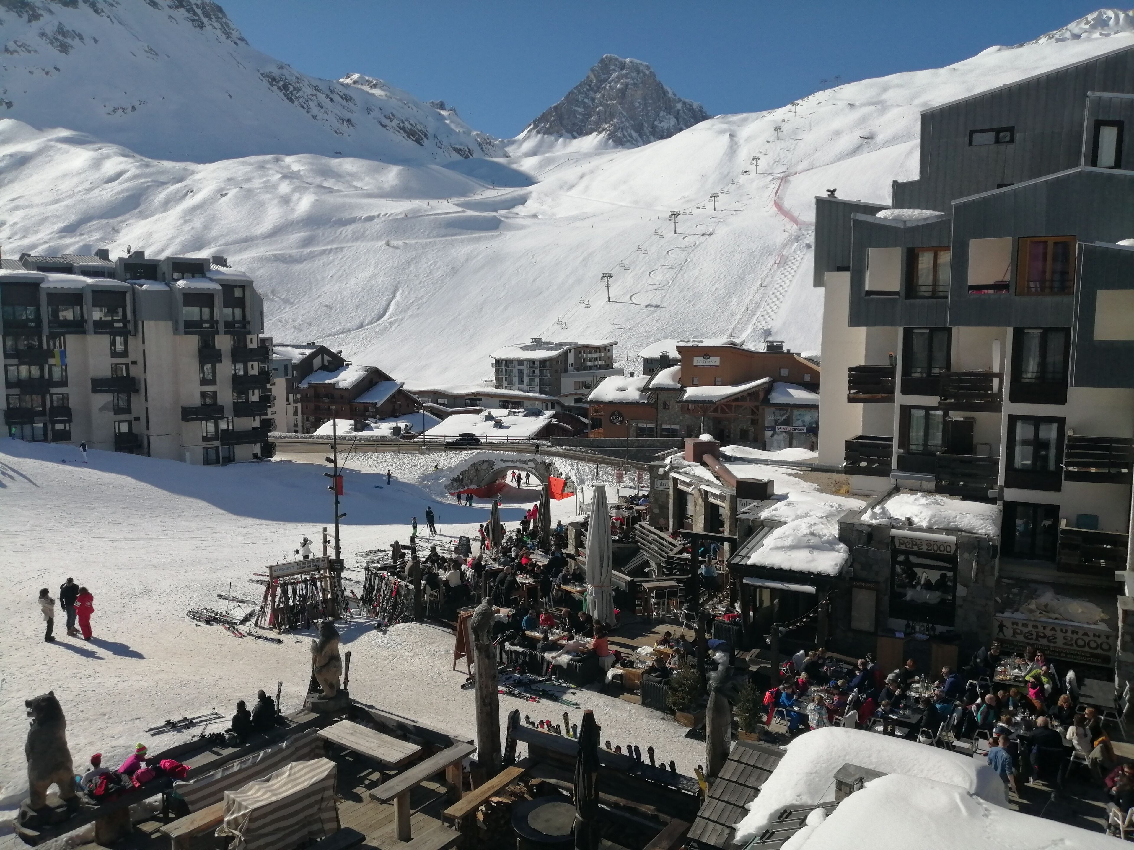 A ski resort with buildings, a ski lift, and a crowd of people.
