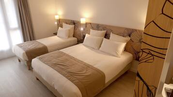 A hotel room with two beds, a wooden headboard with a floral pattern, and a laptop on a side table.