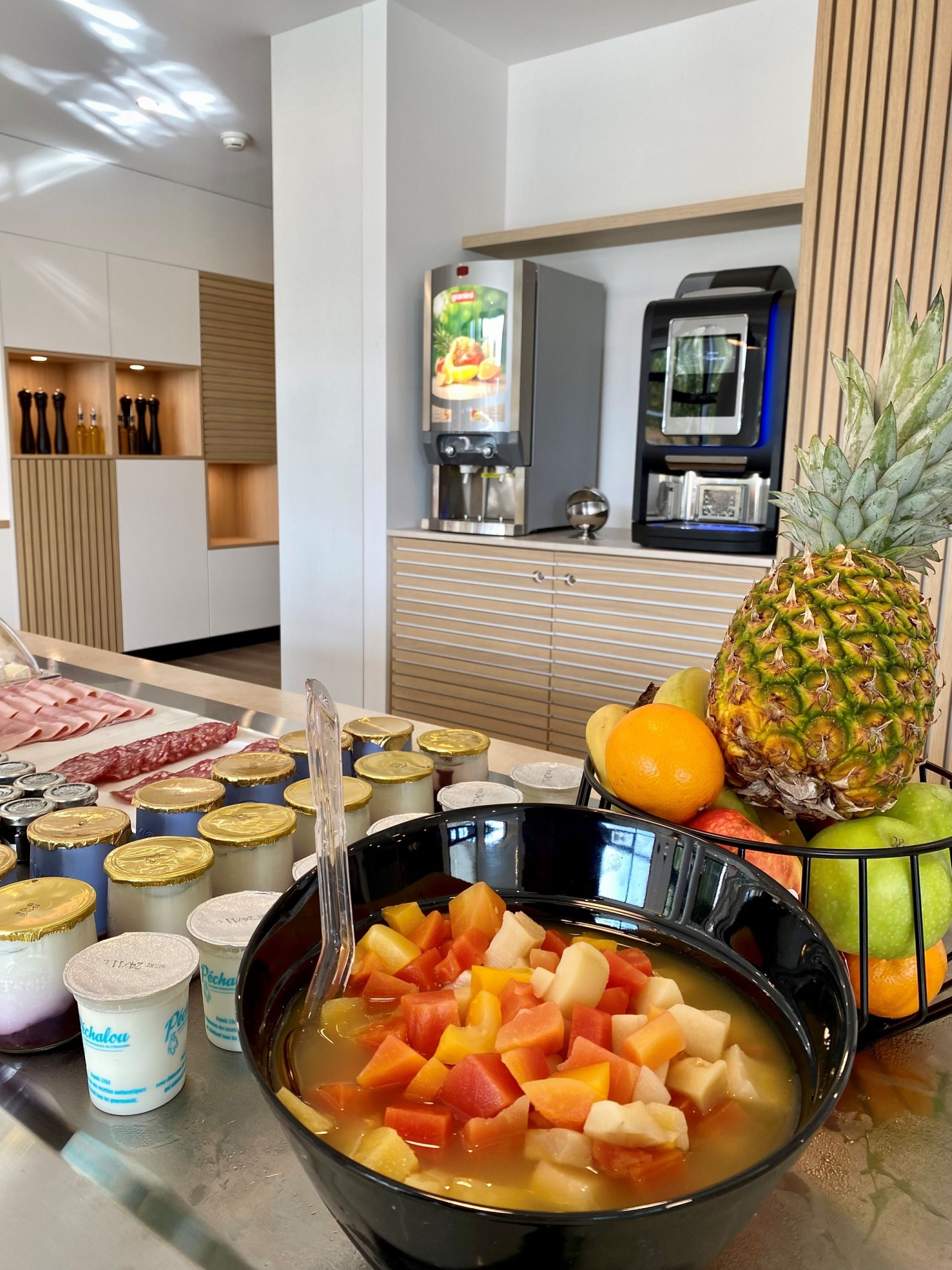 A kitchen counter with a bowl of fruit soup, a pineapple, and various condiments.