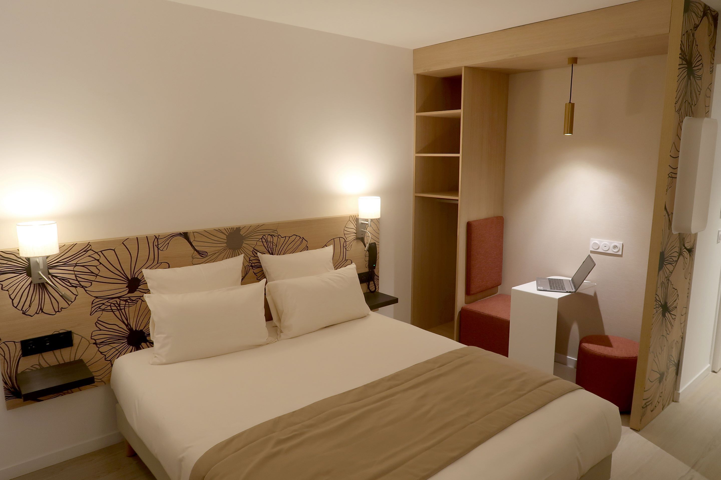 Et moderne hotelværelse med en stor seng, sengeborde med lamper, en bærbar computer på et lille bord og en rød stol.