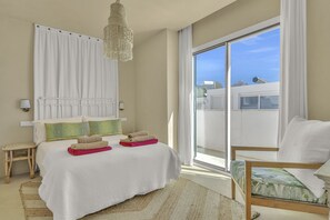 Ein Schlafzimmer mit Bett, Stuhl, Nachttisch, Pendelleuchte und Blick ins Freie.
