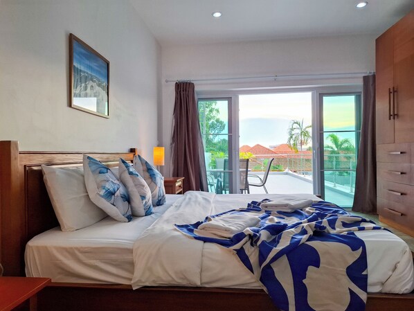 Habitación de hotel con cama, mesita de noche, lámpara, ventana con vistas al exterior y cortina.