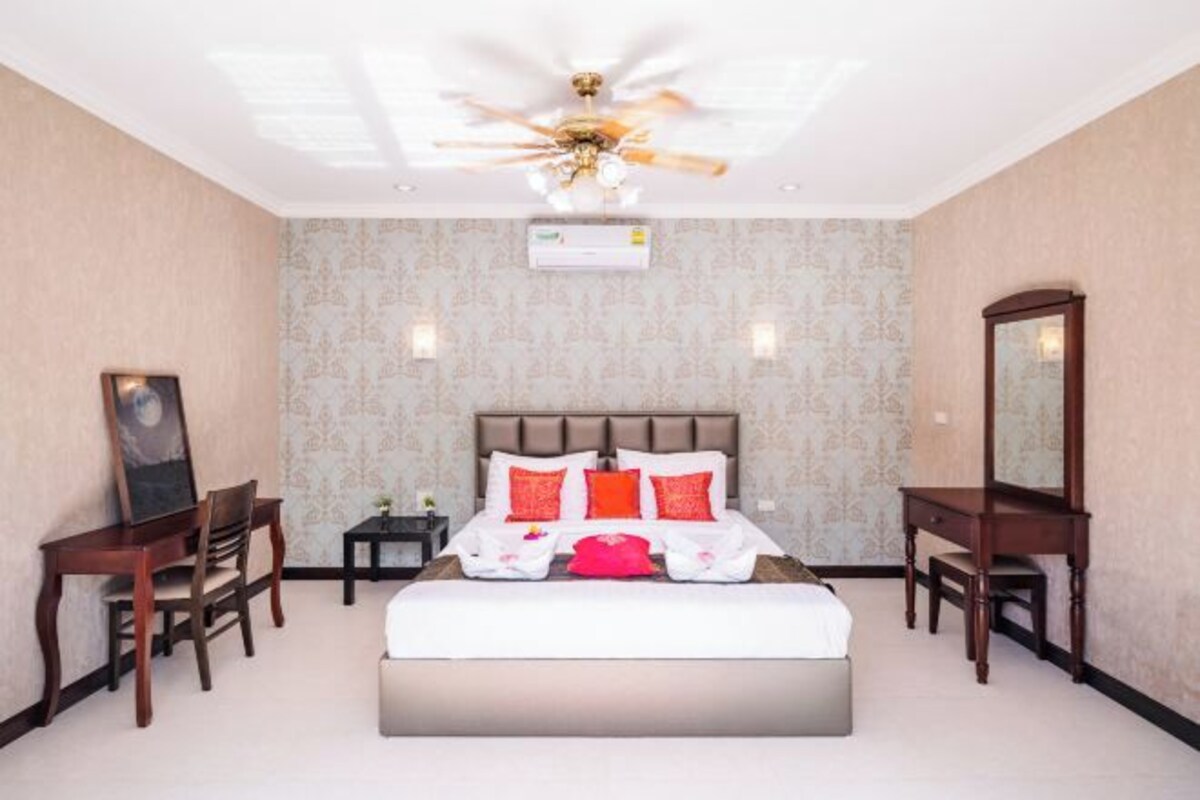 A hotel room with a large bed, a ceiling fan, a bedside table, a chair, a desk, and a mirror.