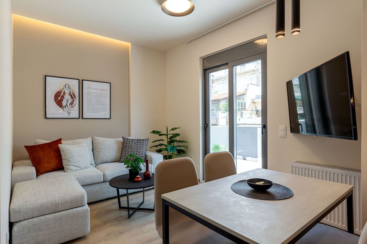 A modern living room with a sofa, a dining table, and a TV mounted on the wall.