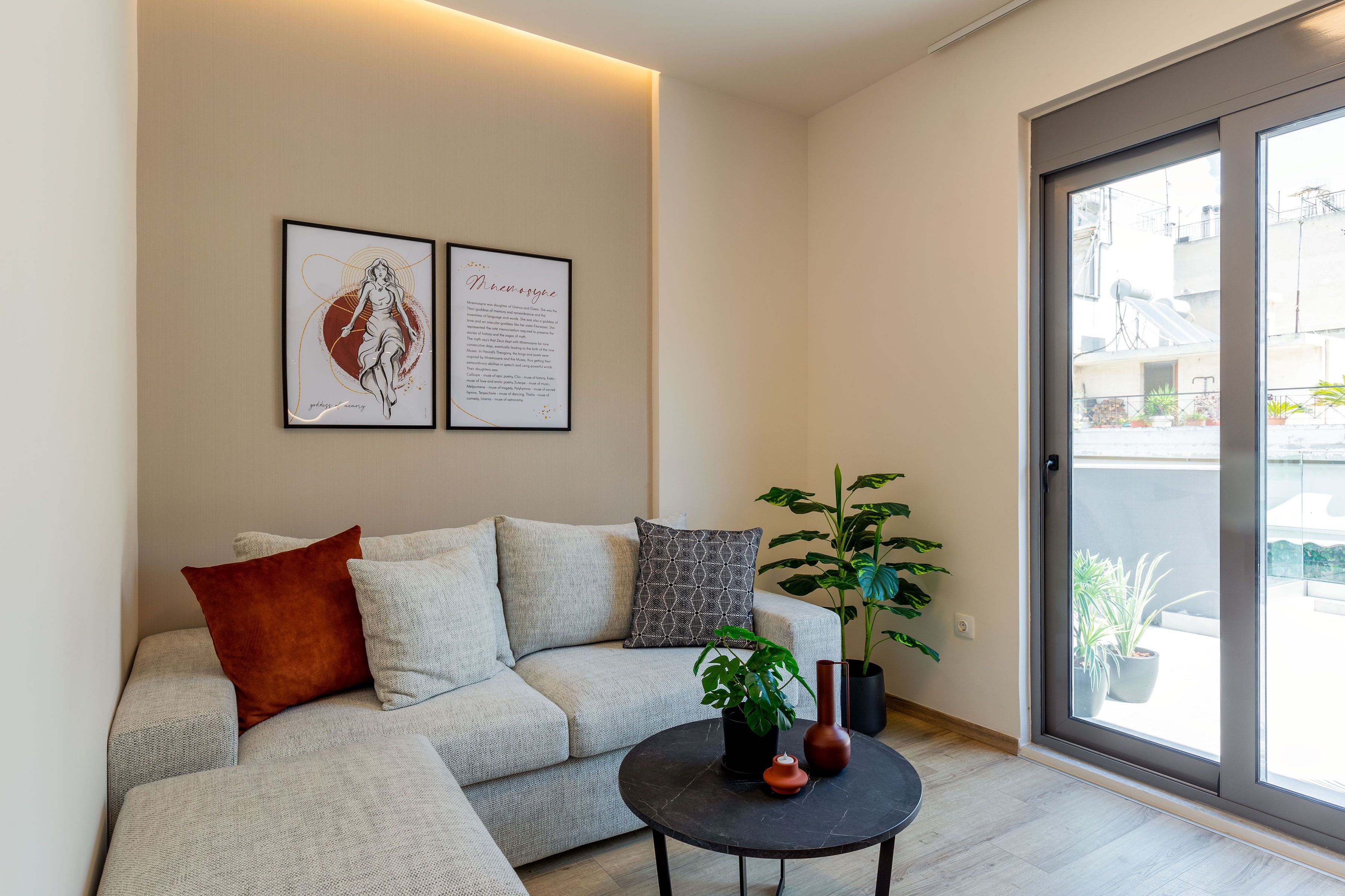 A modern living room with a sofa, two framed artworks, a potted plant, and a sliding glass door leading to an outdoor area.