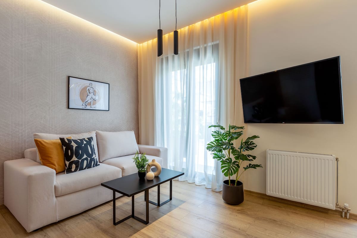 A modern living room with a sofa, a coffee table, a potted plant, and a flat-screen TV mounted on the wall.