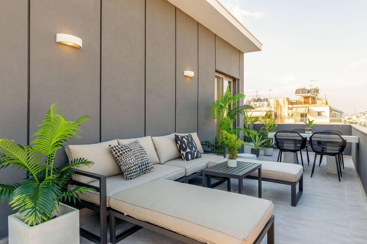 A rooftop terrace with a sofa, lounge chairs, a table, and potted plants.
