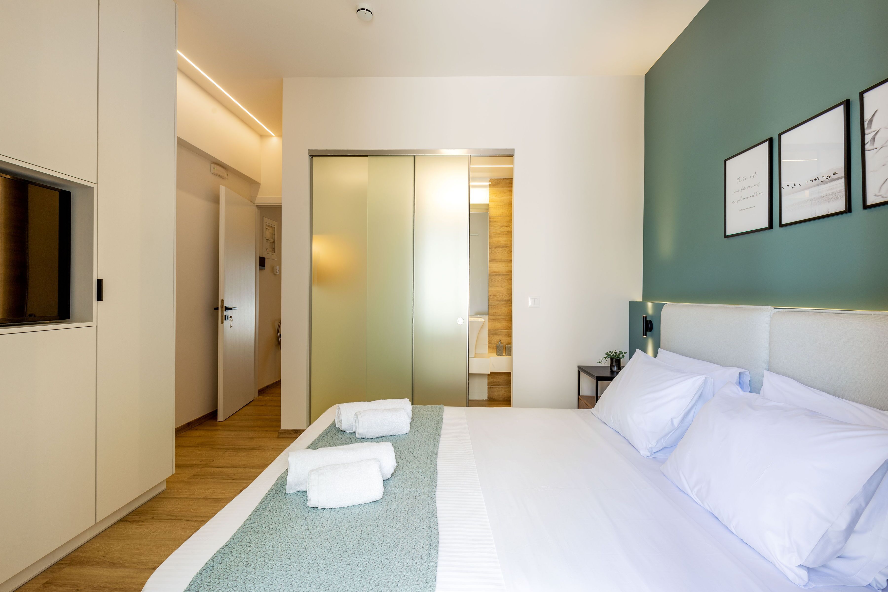 A hotel room with a bed, a TV, a bathroom, and a hallway.