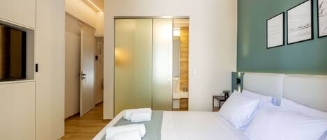 A hotel room with a bed, a TV, a bathroom, and a hallway.
