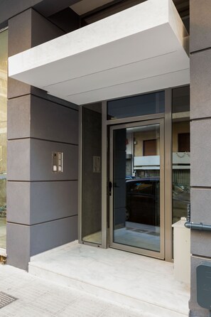 Une entrée moderne avec une porte en verre, un petit espace extérieur et un balcon bien visible.