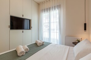 Une chambre d’hôtel avec un lit, un téléviseur fixé au mur, un radiateur et une fenêtre avec des rideaux légers.