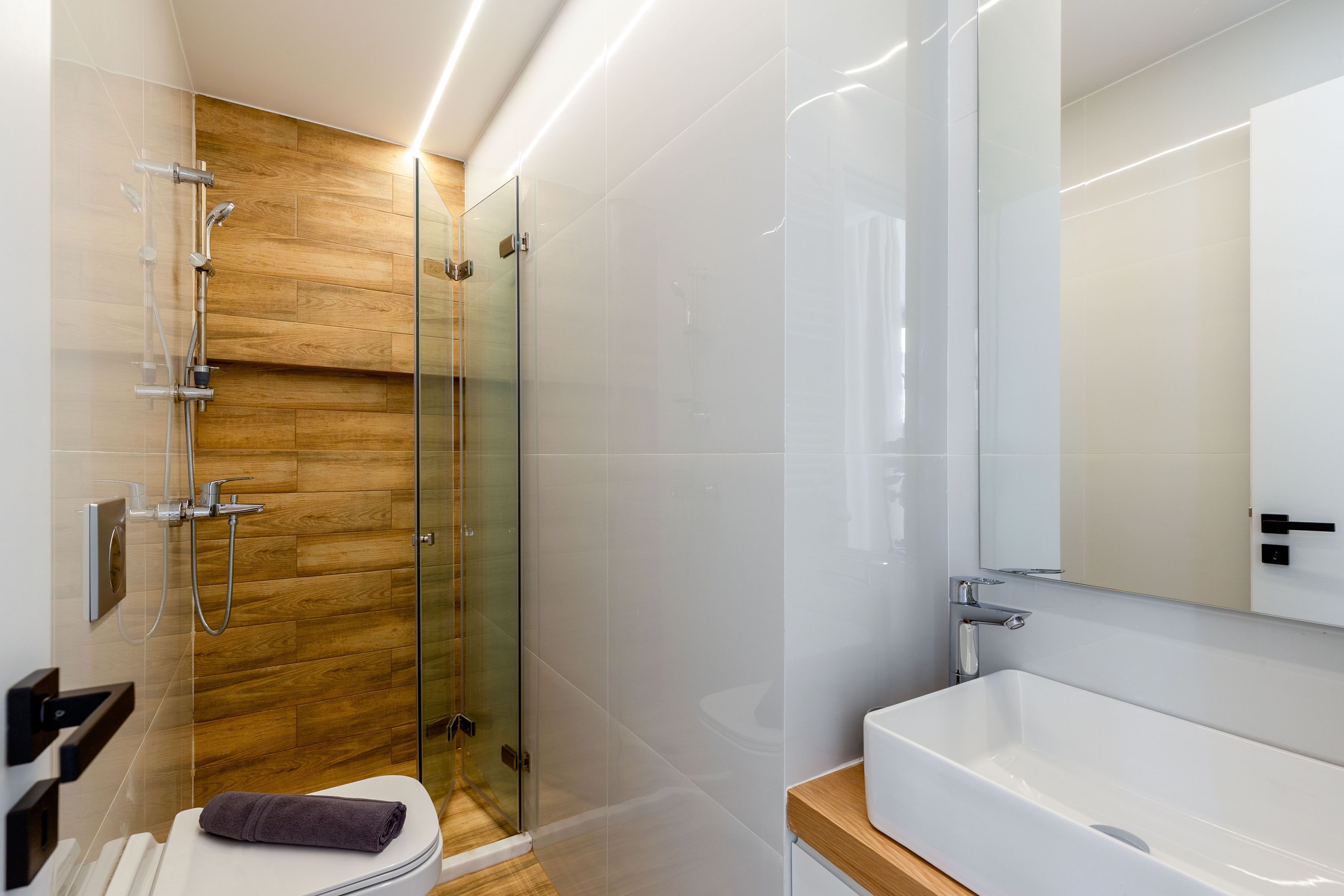 A modern bathroom with a glass-enclosed shower, a white sink, and a wooden vanity.