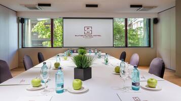 Un salón de conferencias en Suites Plaza Hotel con una larga mesa dispuesta para una reunión, amplias ventanas con vistas a zonas verdes y una pantalla de proyector mostrando el nombre del hotel.