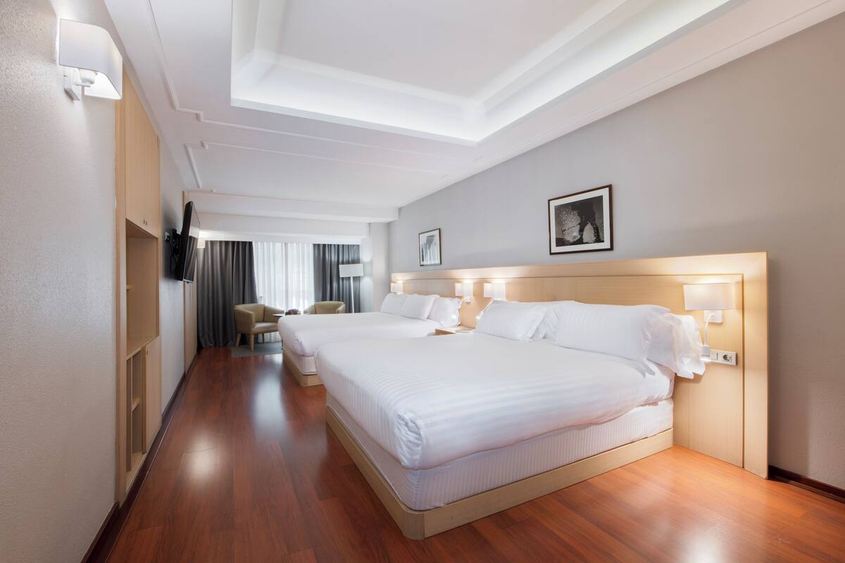 Een hotelkamer met twee bedden, een wandgemonteerde flatscreen televisie en een groot raam met gordijnen.