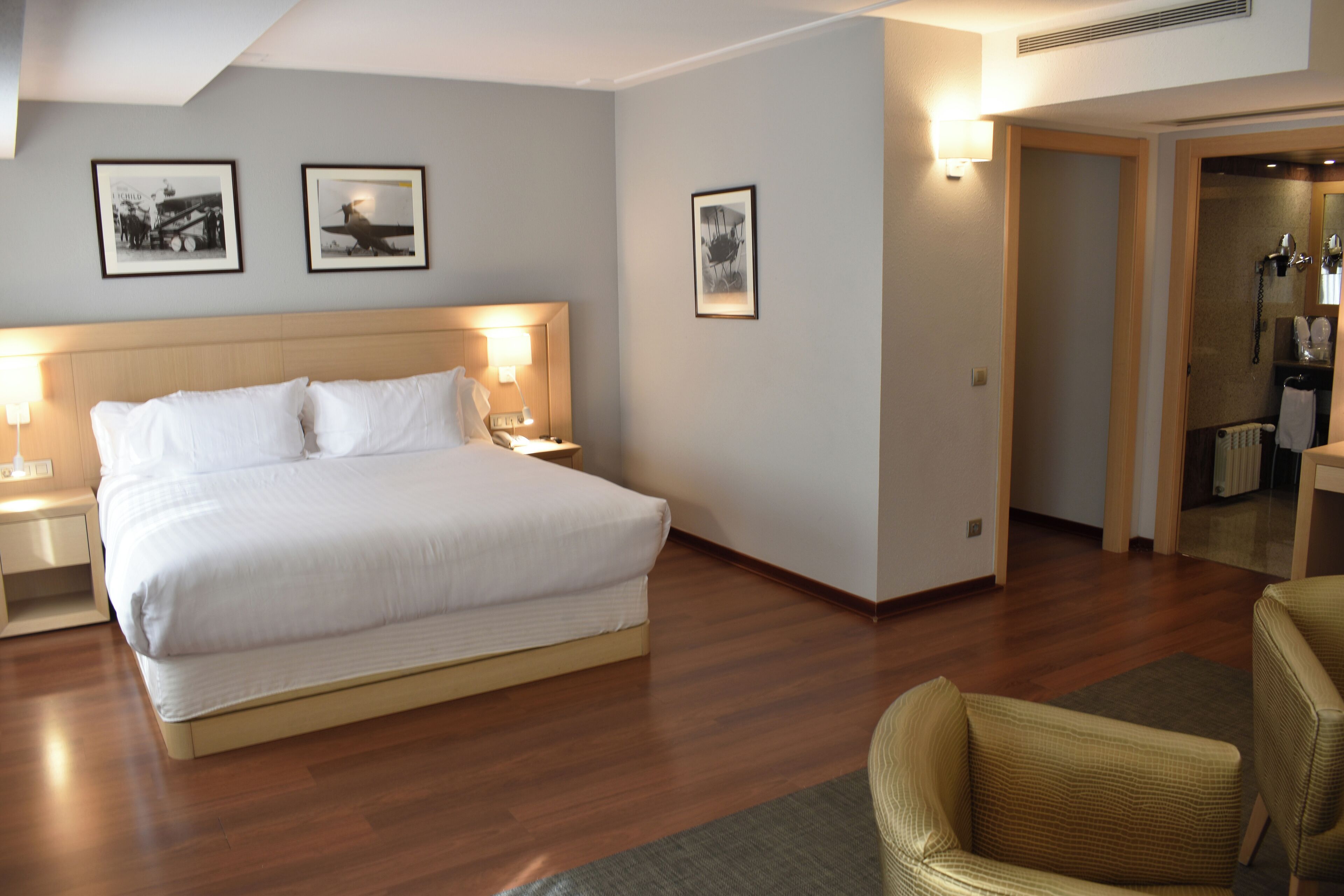 A hotel room with a large bed, two bedside tables with lamps, a chair, and framed pictures on the wall.