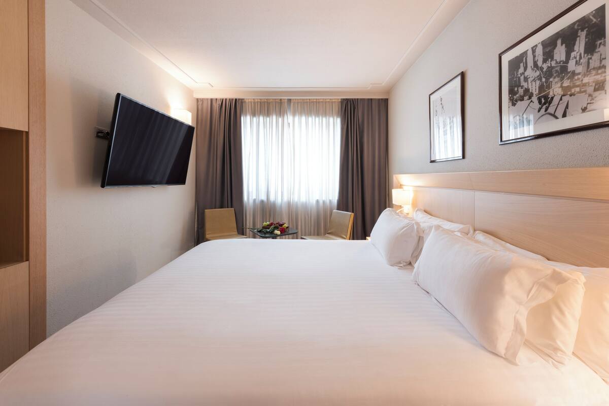 Een hotelkamer met een groot bed, een flatscreen televisie aan de muur, een klein tafeltje met bloemen en een ingelijste foto.