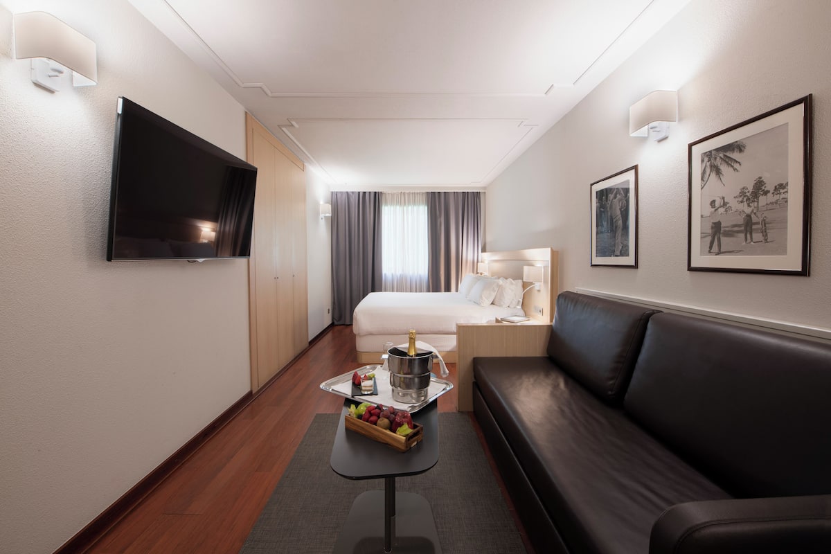 Een hotelkamer met een bed, een televisie, een kleintje tafeltje met fruit, een bank en kunstwerken aan de muur.