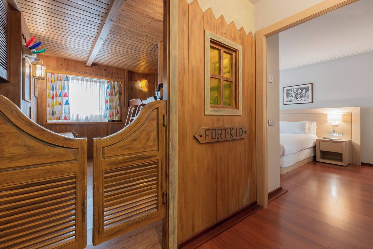Een houten interieur met een bed, nachtkastje en een bord waarop 'FORT-KID' staat.