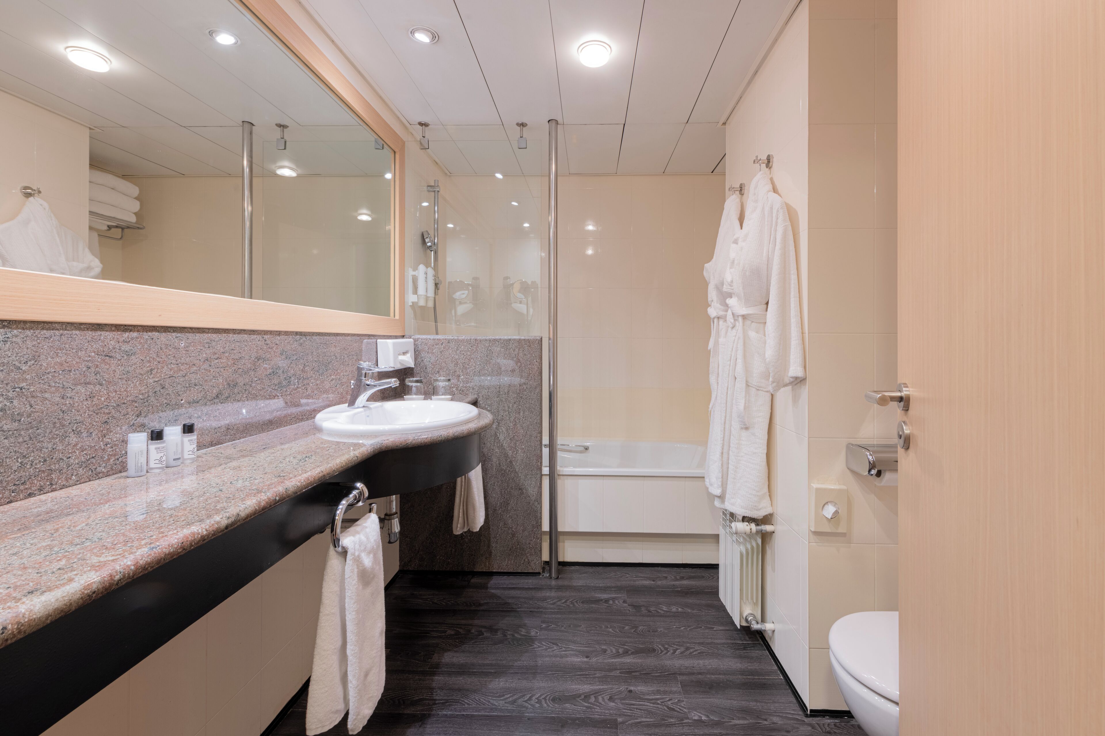A modern bathroom with a granite countertop sink, a large mirror, a bathtub, and a toilet.