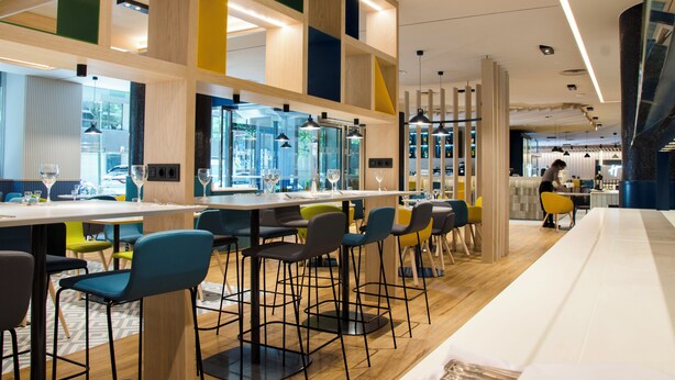 Un espace bar moderne avec des tabourets hauts, un long comptoir et une vue sur la rue.