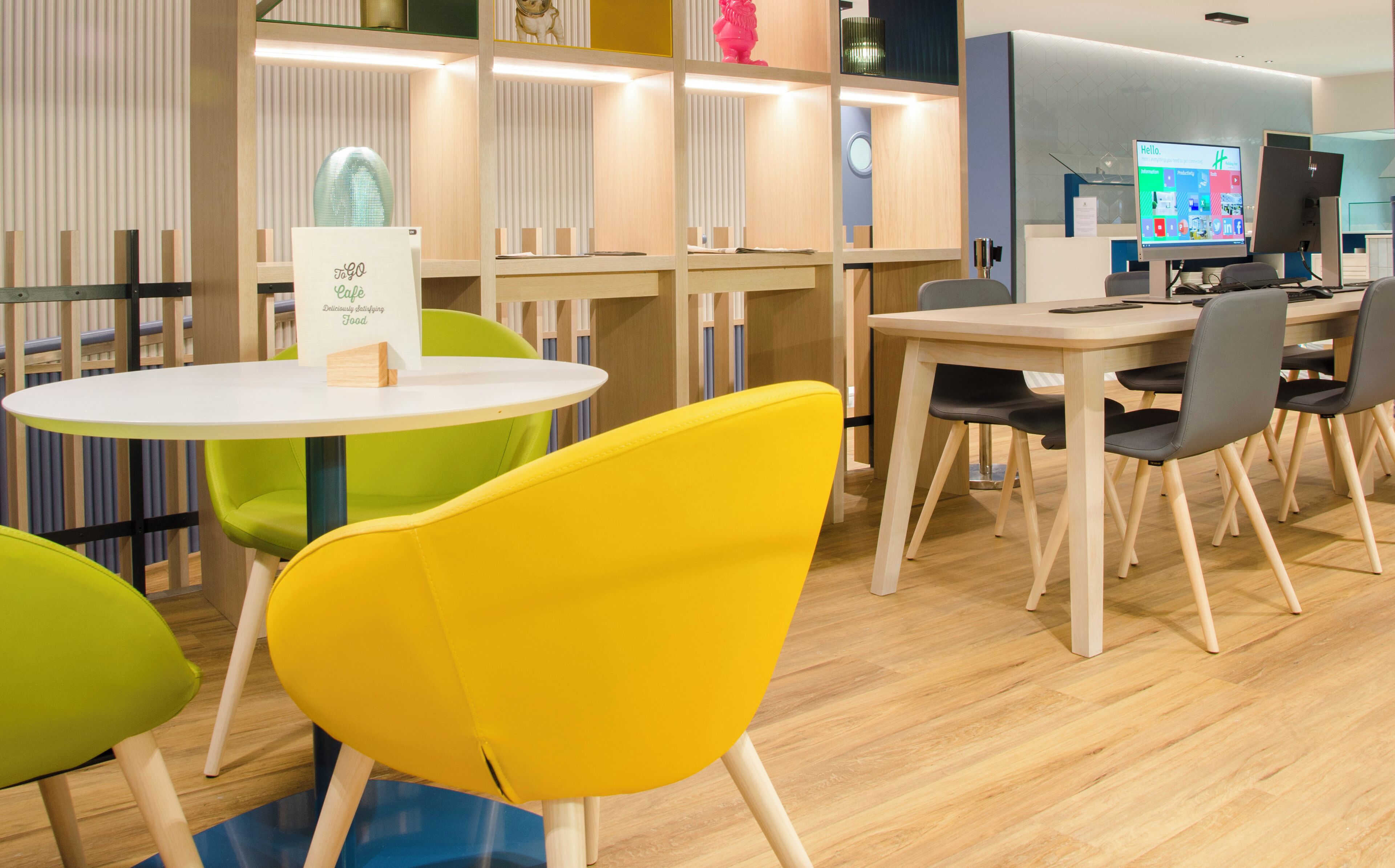 Una cafetería moderna con mesas redondas y sillas coloridas, un menú digital y decoración de madera.