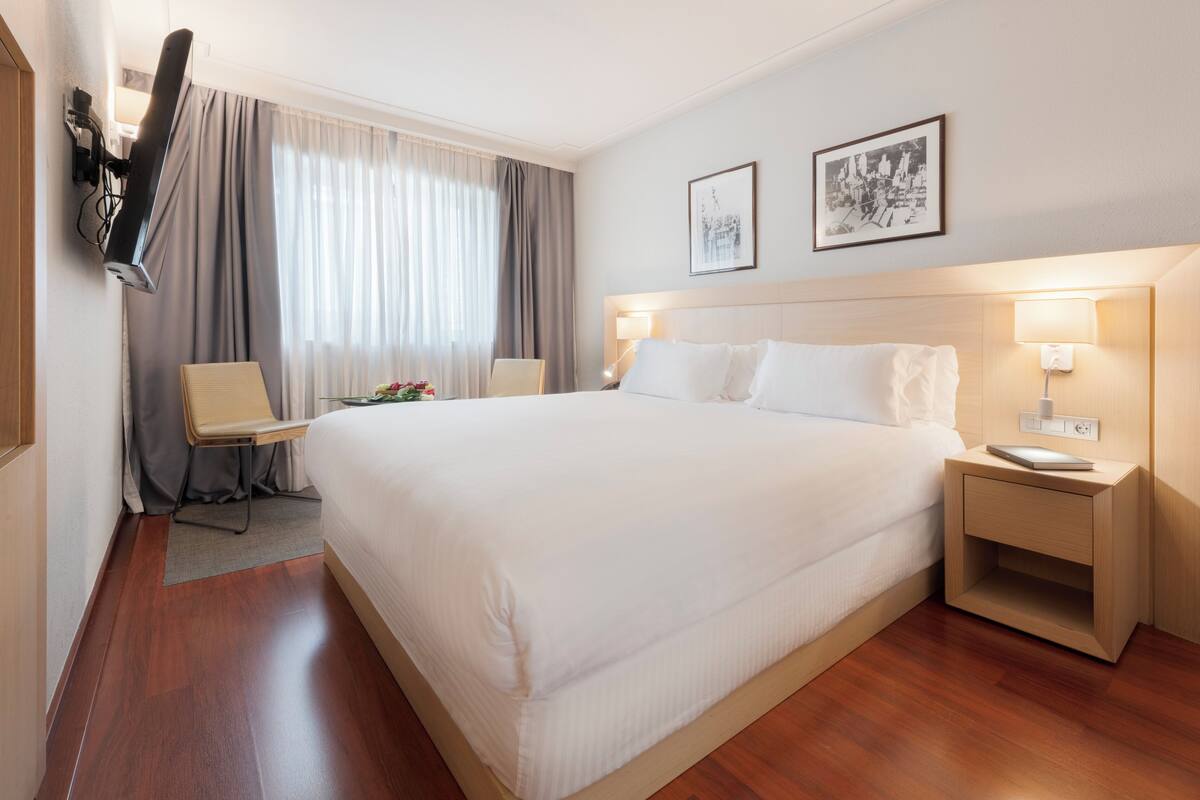 Een hotelkamer met een groot bed, twee bedlampen, een flatscreen televisie aan de muur en een lijst met een afbeelding boven het bed.