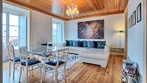 Una sala de estar moderna con techo de madera, un sofá blanco, una mesa de centro de vidrio y un felpudo de cebra.