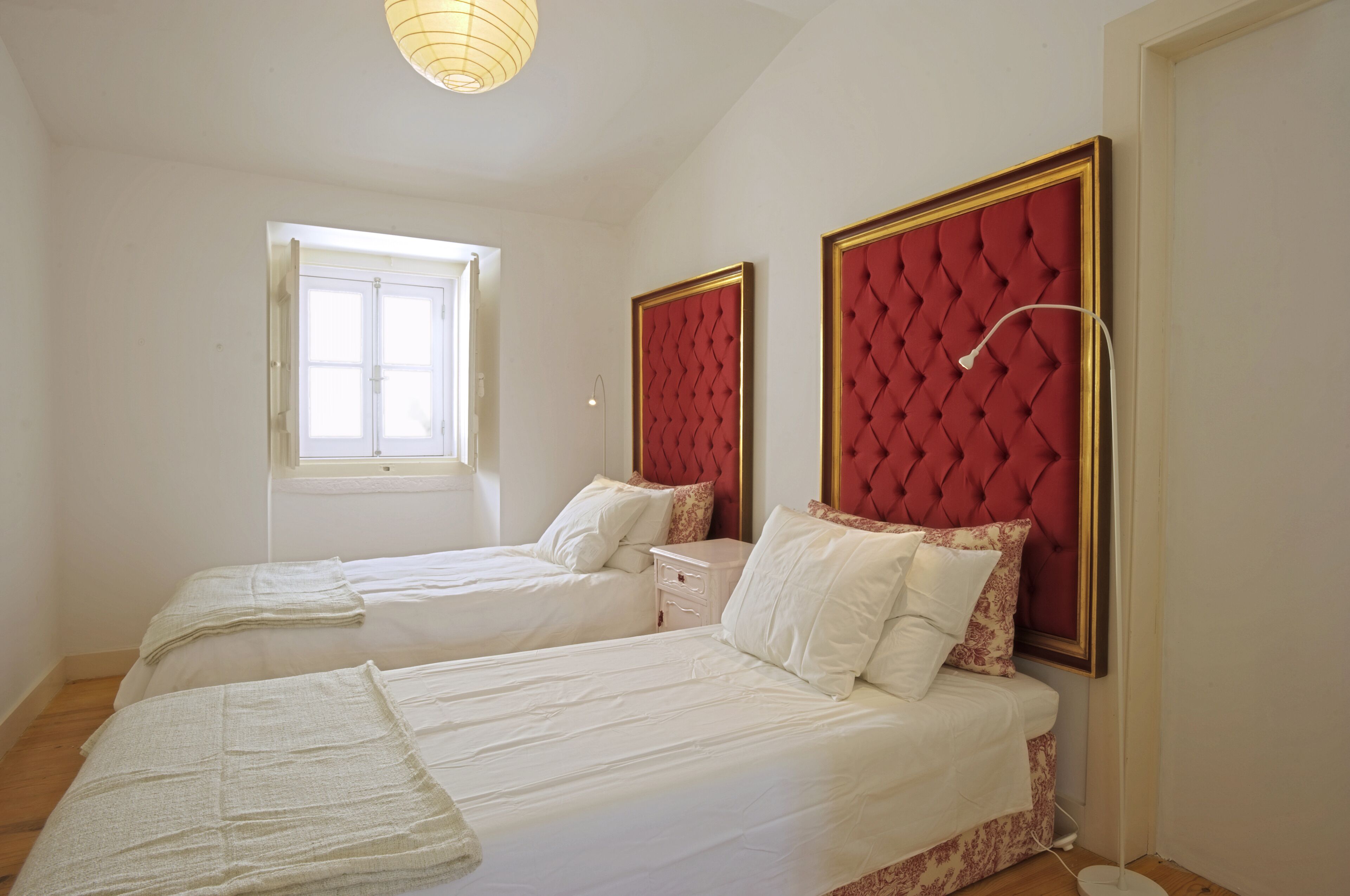 A bedroom with two beds, a window, and a red headboard.