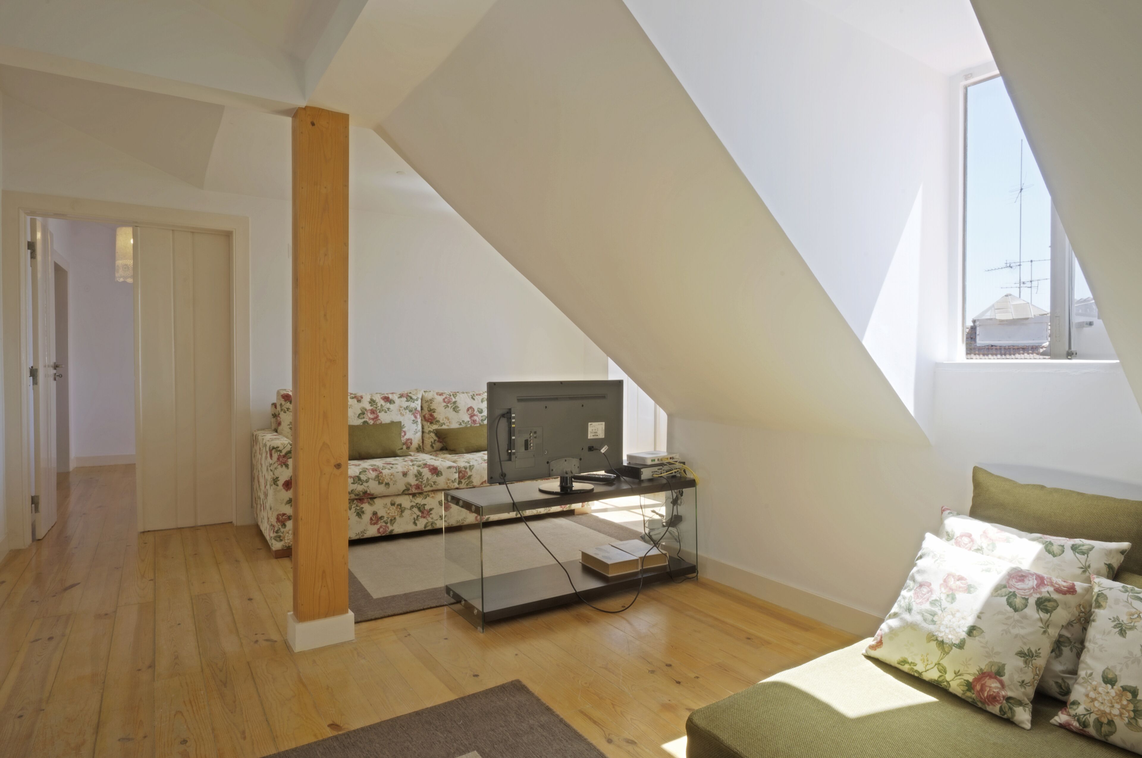 Een moderne loft slaapkamer met een schuine plafond, een glazen bureau, een televisie en een bloemenbank.