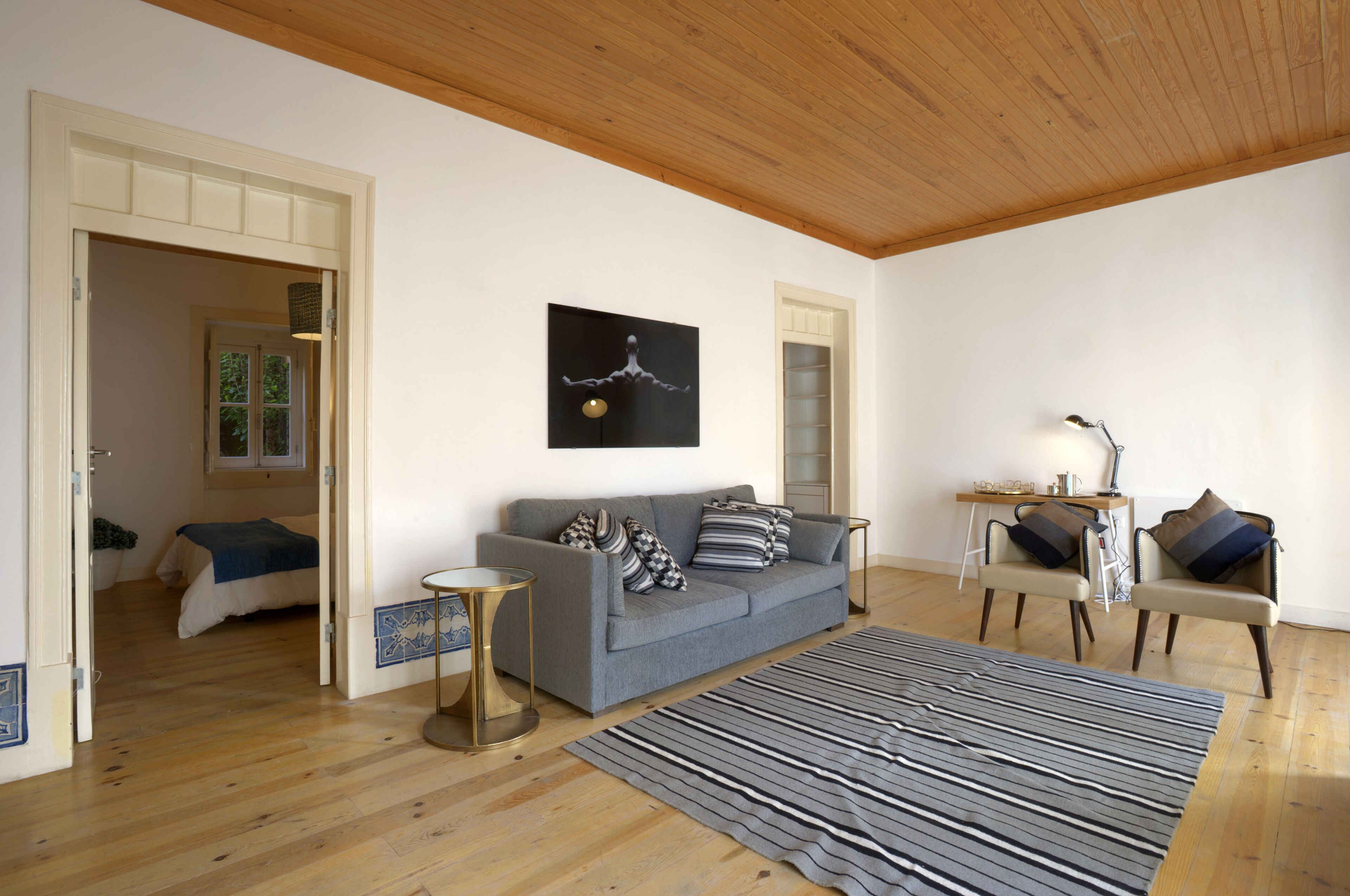 Ein Wohnzimmer mit grauem Sofa, zwei Sesseln, einem Streifen Teppich und einer Holzbalkendecke.