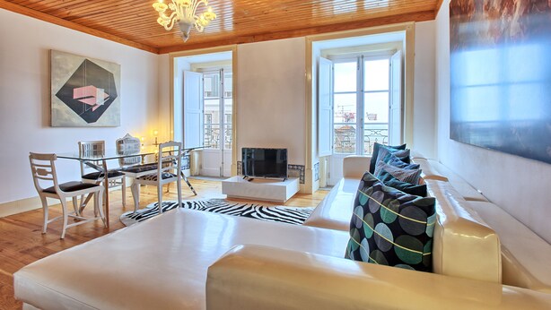 Una sala de estar moderna con techo de madera, una mesa de comedor de vidrio, sofás blancos y un alfombra con estampado de cebra.