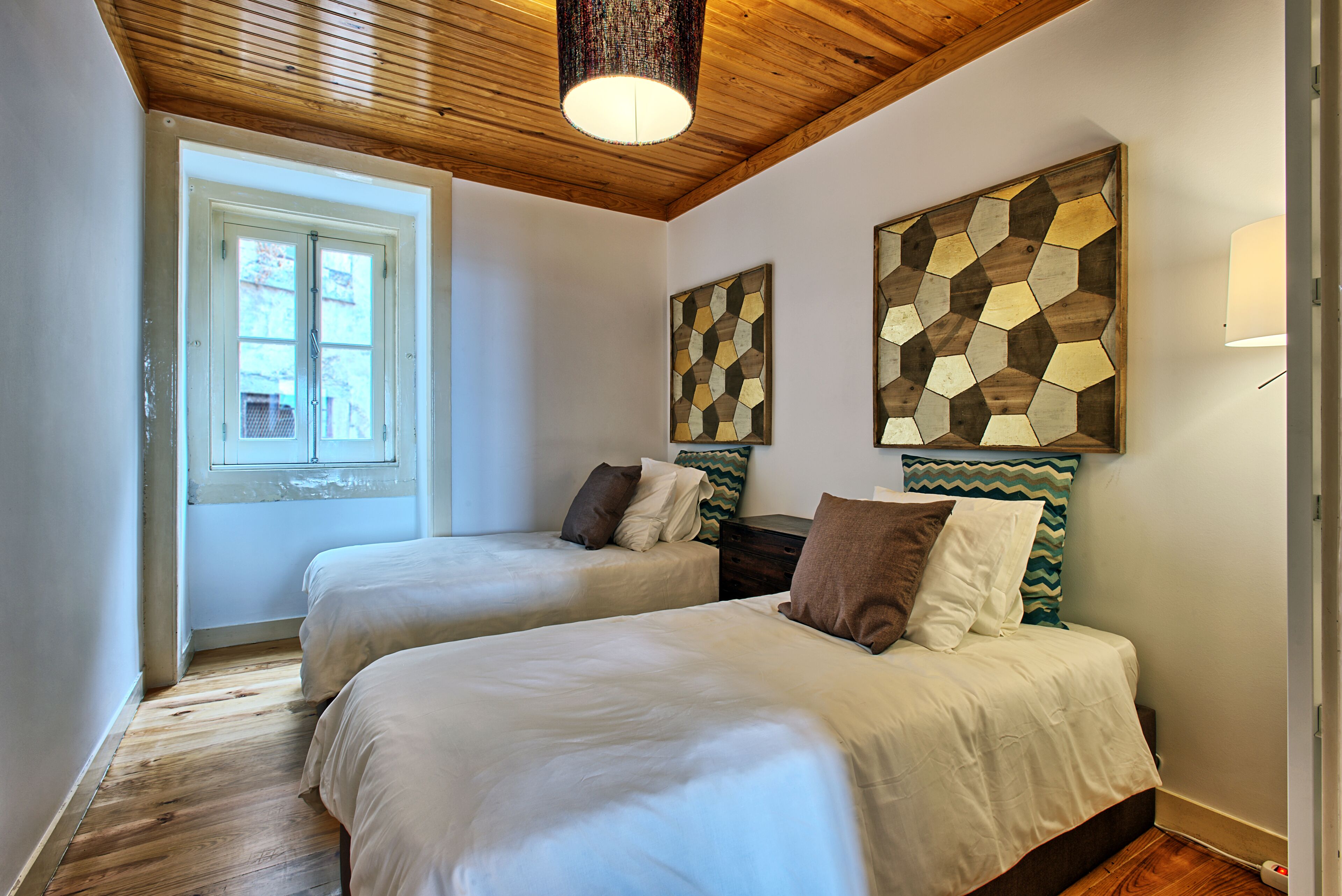 A room with two beds, wooden ceiling, and a window with a view.