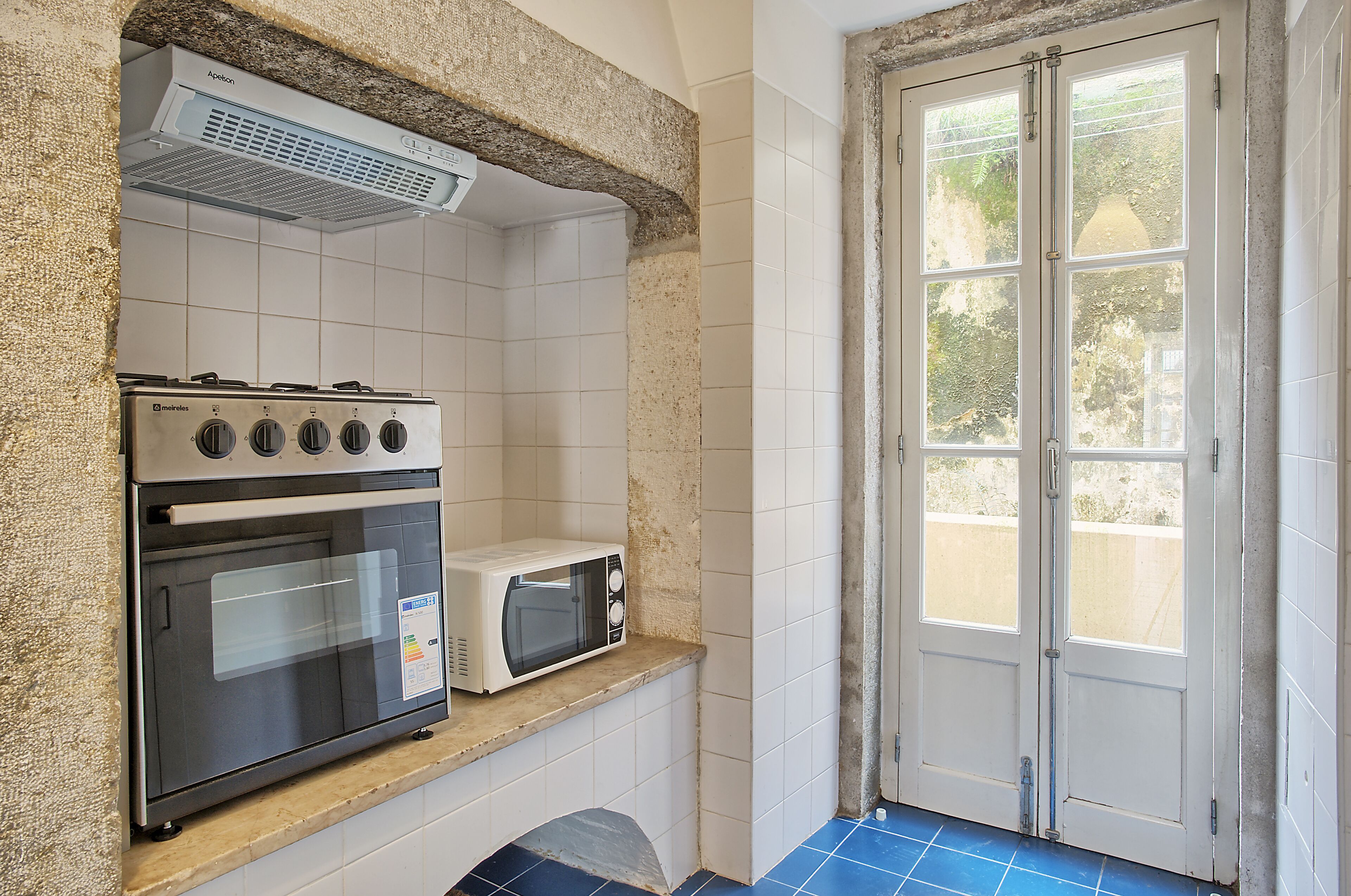 A kitchen with a stove, oven, and microwave on a countertop, a tiled backsplash, and a door leading outside.